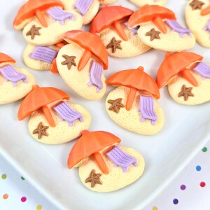 May include: A collection of beach-themed decorative pieces. Each piece features a light yellow base with an orange umbrella, a purple lounge chair, and a brown starfish. The pieces are arranged on a white surface.