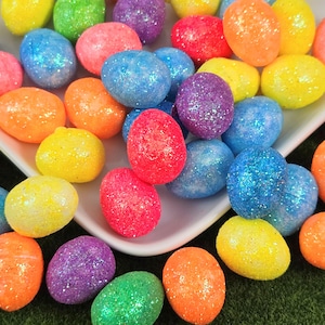 May include: A collection of colorful, glitter-covered Easter eggs in various shades of blue, red, orange, yellow, green, and purple. The eggs are clustered together, creating a festive and vibrant display, perfect for Easter decorations.