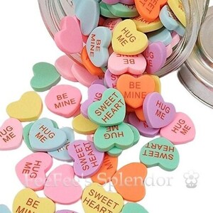 May include: A jar filled with heart-shaped candies with various messages, including "Hug Me", "Sweet Heart", and "Be Mine". The candies are in shades of pink, yellow, green, and blue.