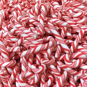 May include: A close-up of a pile of red and white candy canes. The candy canes are all twisted and intertwined, creating a festive and colorful background.