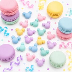 May include: A colorful assortment of macarons and decorative mouse-shaped candies in pastel shades of pink, purple, yellow, blue, and green. The image includes decorative ribbons and confetti, creating a festive and playful aesthetic.