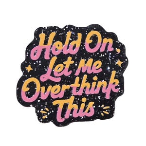 May include: A black glittery enamel pin with an irregular cloud-like shape. The text "Hold On, Let Me Overthink This" is printed in a stylized font, with the top half of the letters in yellow and the bottom half in pink, accented by small stars.