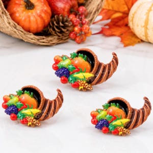 May include: Three cornucopia-shaped ornaments featuring a brown, ribbed horn overflowing with colorful miniature fruits and vegetables, including orange pumpkins, purple grapes, yellow corn, and red berries, all rendered in a glossy finish.