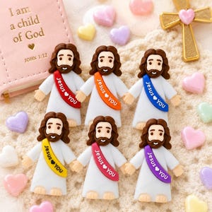 May include: Six small resin figurines of Jesus, each wearing a white robe and a colored sash printed with the text Jesus Loves You. The sashes are red, orange, blue, yellow, pink, and purple. The figurines are arranged with small pastel hearts.