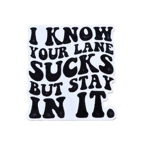 May include: A white sticker with black text that reads "I KNOW YOUR LANE SUCKS BUT STAY IN IT." The text is in a bold, rounded font. The sticker has a wavy, irregular edge.