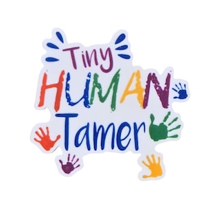 May include: A white die-cut sticker featuring the multicolored text Tiny HUMAN Tamer in various fonts. The design is decorated with small, vibrant handprints in red, blue, green, purple, and yellow, arranged around the central lettering.