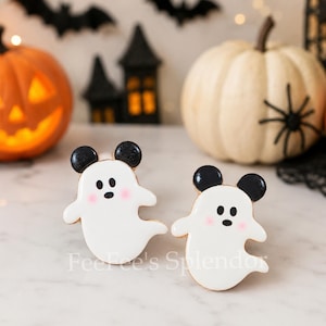 May include: Two ghost-shaped cookies with white icing, black ears, and small black eyes. Each ghost features two pink dots on its cheeks. The text FeeFee's Splendor is visible at the bottom. These treats have a smooth finish and rounded edges.