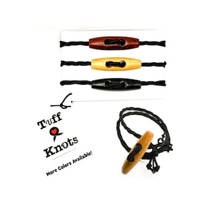 May include: Wooden toggle clasps in brown, natural, and black, with black elastic cords. One clasp is shown with a cord loop. The tag reads "Tuff Knots" and "More Colors Available!"