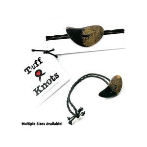 May include: Two handmade hair ties with a distinctive design. Each tie has a dark, curved accent piece in black and brown. The tag reads "Tuff & Knots" with a heart symbol. The image text says "Multiple Sizes Available!"