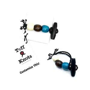Op de afbeelding: Houten kralenarmbanden met witte, bruine en turquoise kralen, en een zwarte toggle sluiting. De armbanden worden gepresenteerd op witte labels met de tekst "Tuff Knots" en "Customize This!"