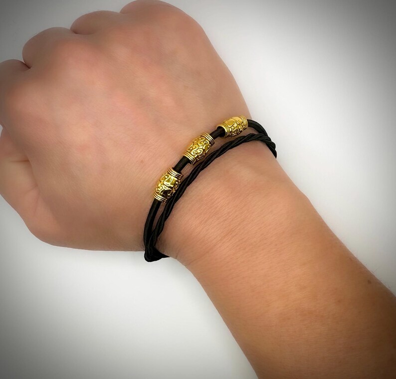 Peut inclure: Un bracelet en cuir noir avec des perles dor&eacute;es. Les perles ont un design textur&eacute;.