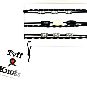 Peut inclure: Ensemble de quatre &eacute;lastiques &agrave; cheveux tress&eacute;s noirs avec des perles argent&eacute;es et noires. Les &eacute;lastiques &agrave; cheveux sont emball&eacute;s sur une carte blanche avec le texte "Tuff Knots Stylish Handmade Hair Ties".
