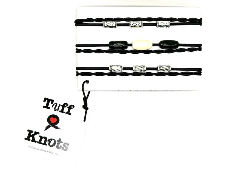 Peut inclure: Ensemble de quatre &eacute;lastiques &agrave; cheveux tress&eacute;s noirs avec des perles argent&eacute;es et noires. Les &eacute;lastiques &agrave; cheveux sont emball&eacute;s sur une carte blanche avec le texte "Tuff Knots Stylish Handmade Hair Ties".