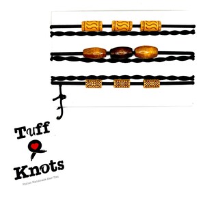 Peut inclure: Ensemble de trois &eacute;lastiques &agrave; cheveux noirs avec des perles en bois. Les perles sont brunes, orange et ont un motif g&eacute;om&eacute;trique. Les &eacute;lastiques &agrave; cheveux sont &eacute;tiquet&eacute;s "Tuff Knots -  Handmade Hair Ties".