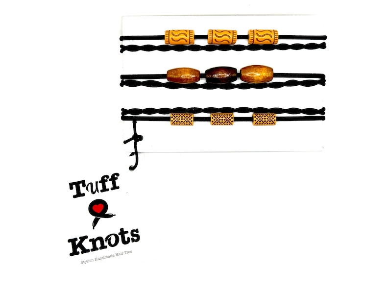 Peut inclure: Ensemble de trois &eacute;lastiques &agrave; cheveux noirs avec des perles en bois. Les perles sont brunes, orange et ont un motif g&eacute;om&eacute;trique. Les &eacute;lastiques &agrave; cheveux sont &eacute;tiquet&eacute;s "Tuff Knots -  Handmade Hair Ties".