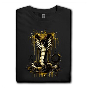 May include: Black t-shirt with a cobra graphic in gold and black. The cobra has red eyes and is surrounded by gold paint splashes. The shirt is a Gildan brand.