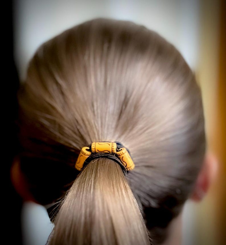 Peut inclure: Une queue de cheval brune avec un &eacute;lastique noir et des perles en bois brun.