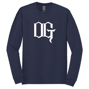 May include: Navy blue long-sleeve shirt with the white letters "OG" in a gothic font. The shirt is made of a soft material and has a crew neck.