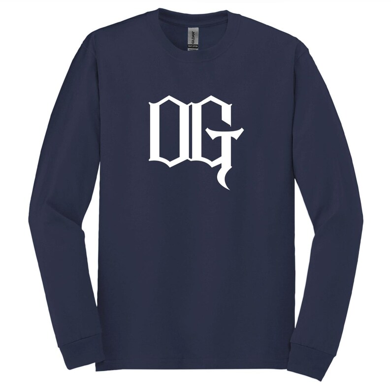 May include: Navy blue long-sleeve shirt with the white letters "OG" in a gothic font. The shirt is made of a soft material and has a crew neck.