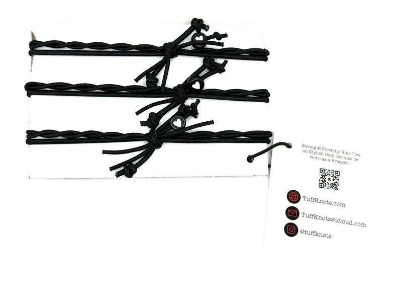 Peut inclure: Trois &eacute;lastiques &agrave; cheveux tress&eacute;s noirs avec de petits charmes en forme de c&oelig;ur noirs. Les &eacute;lastiques &agrave; cheveux sont emball&eacute;s sur une carte blanche avec un code QR et le texte "Strong & Stretchy Hair Ties so stylish they can also be worn as a Bracelet!"  TuffKnots.com TuffKnots@icloud.com @tuffknots