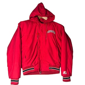 May include: A bright red hooded jacket featuring a front zipper closure with snap buttons, long sleeves with ribbed cuffs, and a ribbed hem. The word GEORGIA is embroidered in white and black on the chest, and a Starter logo is on the left sleeve.