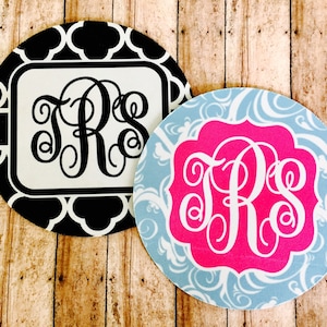 May include: Two round coasters with different patterns. One coaster has a black and white geometric pattern with a white monogram "TRS" in the center. The other coaster has a blue and white swirl pattern with a pink monogram "TRS" in the center.