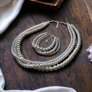 May include: A set of pearl jewelry featuring a multi-strand necklace and a matching bracelet. The necklace and bracelet are made of white pearls and have a classic design.