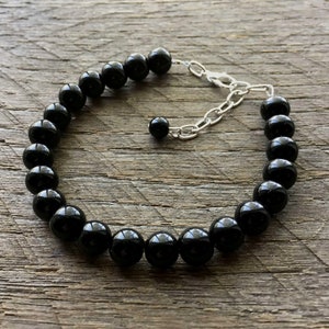 May include: A black onyx beaded bracelet with a silver chain clasp. The bracelet is made of round, smooth beads and is approximately 7 inches in length.