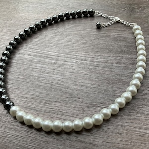 May include: A black and white beaded necklace with a silver clasp. The necklace is made of round beads, with the black beads on one half and the white beads on the other half.