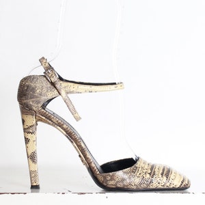 May include: A pair of high-heeled shoes with a snakeskin pattern. The shoes have a strap that goes around the ankle and a pointed toe.