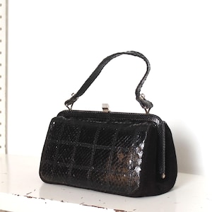 Pode incluir: Uma bolsa preta vintage com formato retangular estruturado. A frente apresenta um padrão quadriculado e as laterais são de camurça preta. Possui uma pequena alça e um fecho prateado.