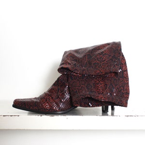 May include: A pair of brown and black snakeskin boots with a slouchy, folded-over top. The boots have a pointed toe and a low heel.