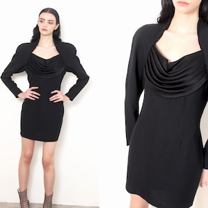 May include: A black dress with a draped cowl neckline and long sleeves. The dress has a fitted silhouette and is paired with a matching bolero jacket with structured shoulders. The outfit is a classic, elegant style.