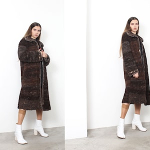 May include: A long brown and black fuzzy coat with a zipper closure. The coat has a collar and is worn by a person with white boots.