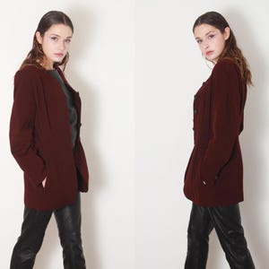 May include: A burgundy blazer with long sleeves and a button closure. The blazer has a fitted silhouette and is worn by a person with dark hair.