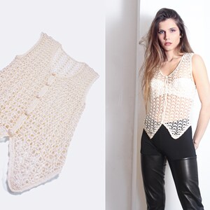 May include: A white crocheted sleeveless top with a button closure. The top has a delicate, open-weave pattern and a slightly pointed hem.
