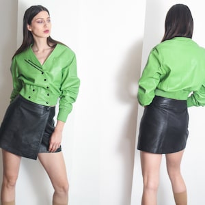 Peut inclure: Une veste en cuir vert avec des finitions noires et une jupe en cuir noir. La veste a une fermeture à boutons et la jupe a un design enveloppant.