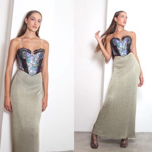 May include: A strapless corset top with a floral design and a long, shimmering gold skirt. The corset features black lace trim and a sweetheart neckline. The skirt is floor-length and has a subtle sheen. The outfit is a vintage style.