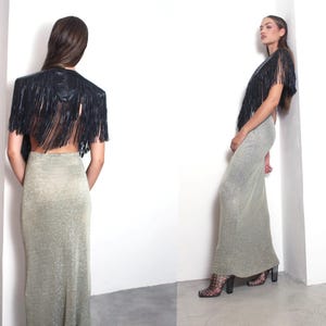 May include: A black fringed bolero jacket and a long, shimmering silver-gold skirt. The jacket features a structured shoulder and a cascade of fringe. The skirt is form-fitting and floor-length, creating a glamorous ensemble.