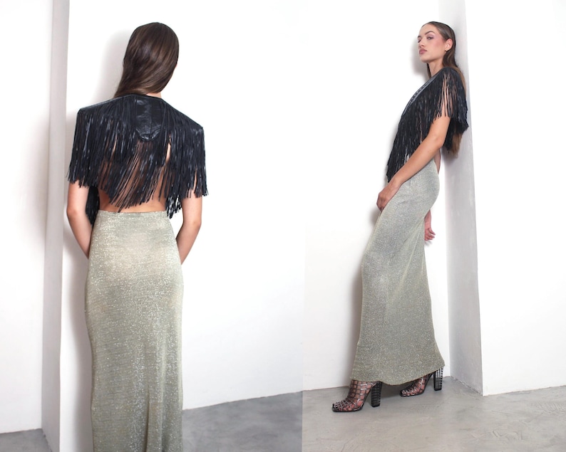 May include: A black fringed bolero jacket and a long, shimmering silver-gold skirt. The jacket features a structured shoulder and a cascade of fringe. The skirt is form-fitting and floor-length, creating a glamorous ensemble.