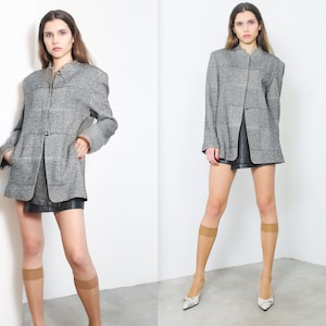 May include: A gray and black checkered blazer with a mandarin collar and a single button closure. The blazer is worn over a black skirt and the model is wearing nude stockings and heels.