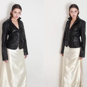 May include: A black leather jacket with a fitted silhouette and a white satin skirt. The jacket has a notched collar, long sleeves, and a front button closure.