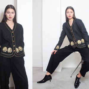 May include: A black linen jacket with gold lion embroidery and a v-neck collar. The jacket has a button closure and gold trim.