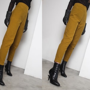 May include: A person wearing a pair of mustard yellow pants and black ankle boots. The person is wearing black leather gloves.