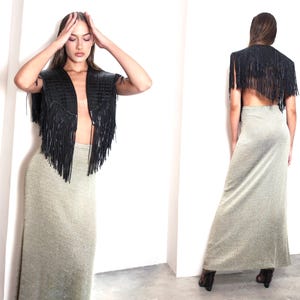 May include: A black leather fringe vest and a long, shimmering silver-grey skirt. The vest has a V-neck design and the skirt is floor-length. The outfit is styled against a white background.