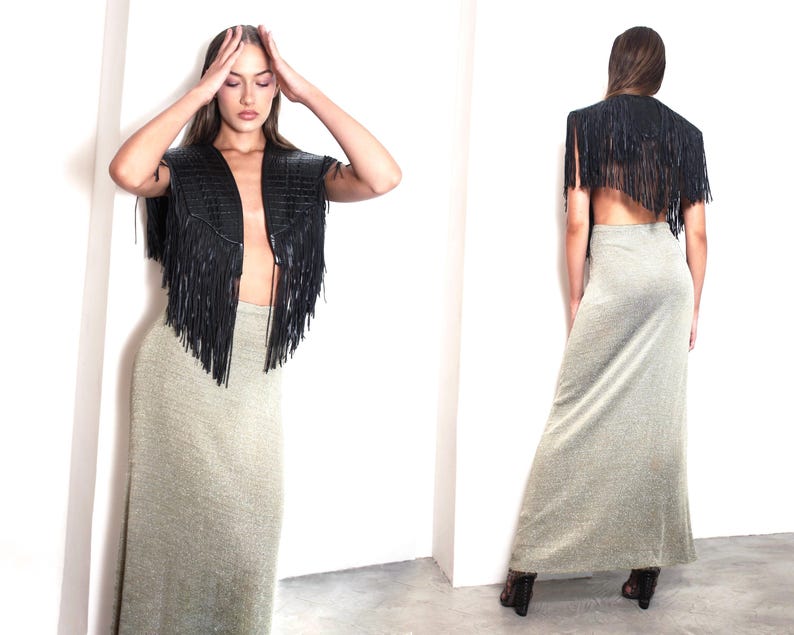 May include: A black leather fringe vest and a long, shimmering silver-grey skirt. The vest has a V-neck design and the skirt is floor-length. The outfit is styled against a white background.
