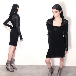 May include: A black, textured knit dress with long sleeves and a square neckline. The dress is knee-length and paired with patterned ankle boots. The model is standing in front of a white background.