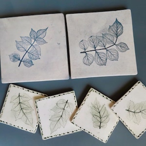 May include: Set of six square coasters with a leaf design. The coasters are white with a blue or green leaf design. The coasters have a decorative border.