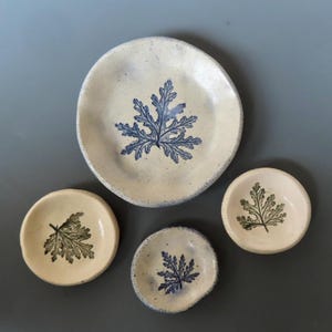 May include: Set of four ceramic dishes with a leaf design. The dishes are white with blue and green leaf patterns.