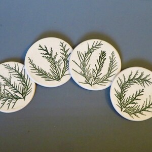 May include: Set of four white ceramic coasters with a green fern design.